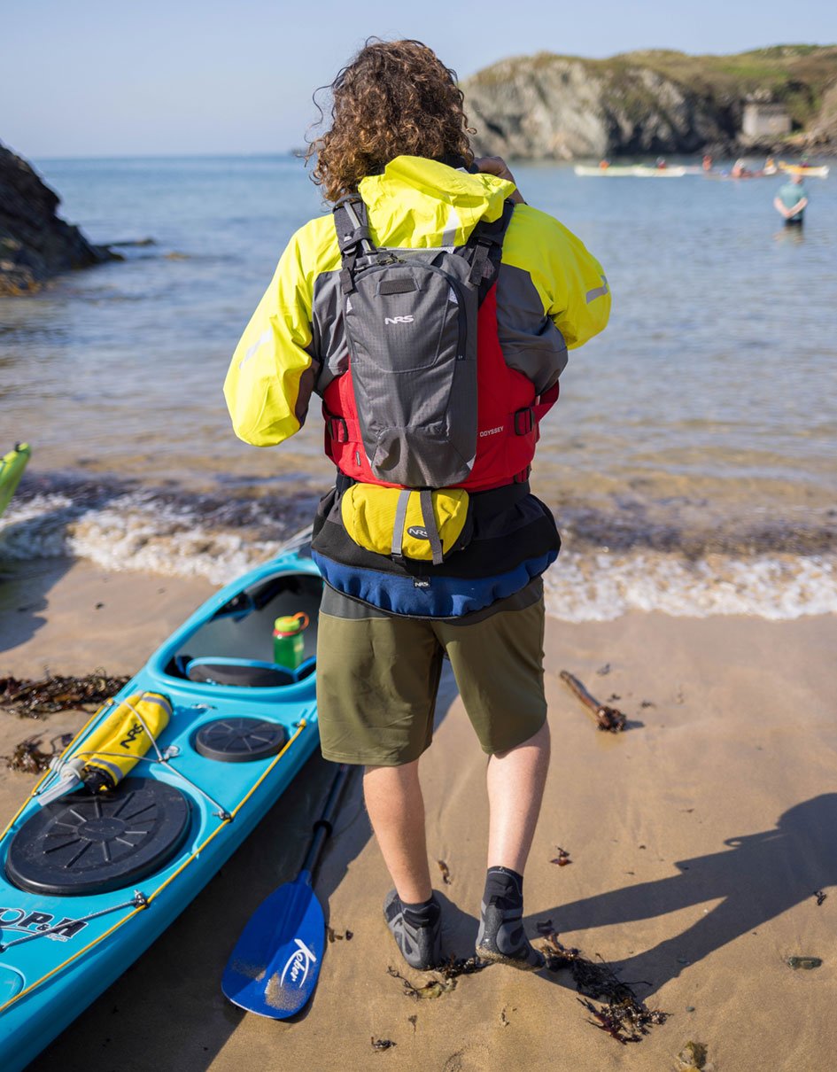 person wearing NRS Wetshoe while standing on sand beach beside a kayak