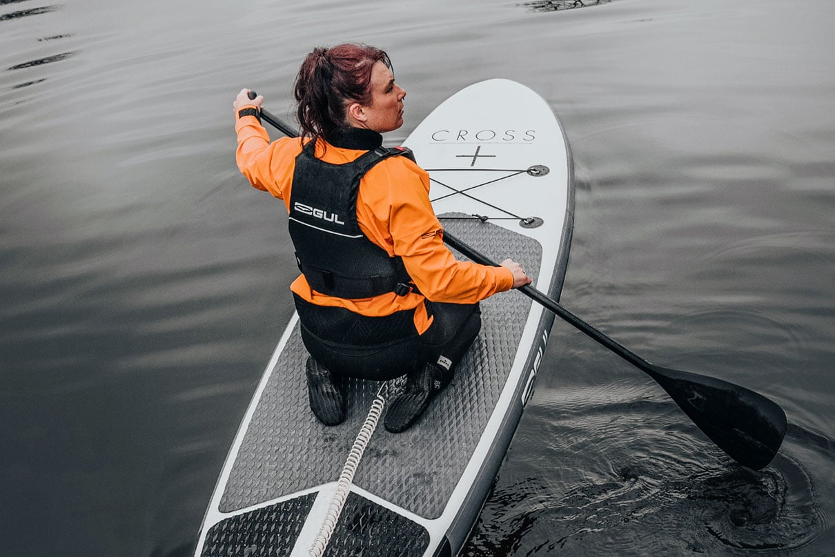 woman paddles inflatable SUP while wearing GUL Power Boots