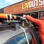 Persons using cam strap to show how to transport a paddleboard.