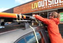 Persons using cam strap to show how to transport a paddleboard.