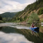Man paddling an inflatable kayak on river.