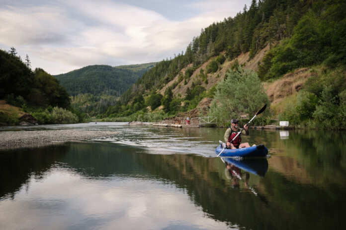 Man paddling an inflatable kayak on river.