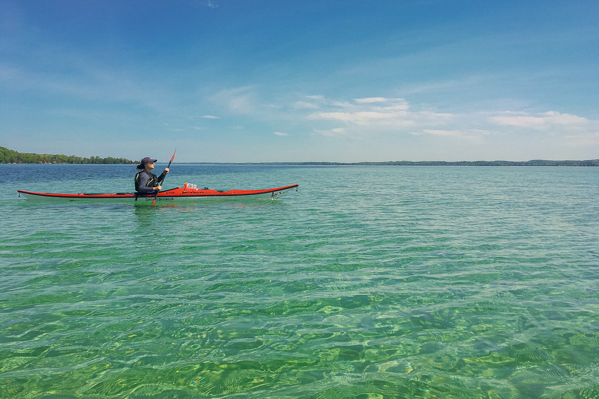 A kayaker floats on crystal clear torch lake at the mouth of the Torch River in Michigan