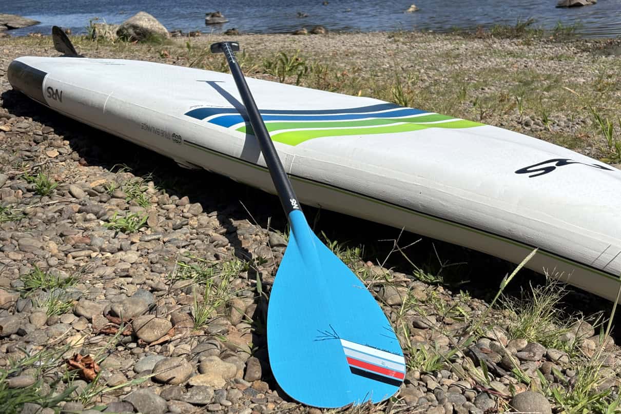 An adjustable SUP paddle on top of a paddleboard near the water.